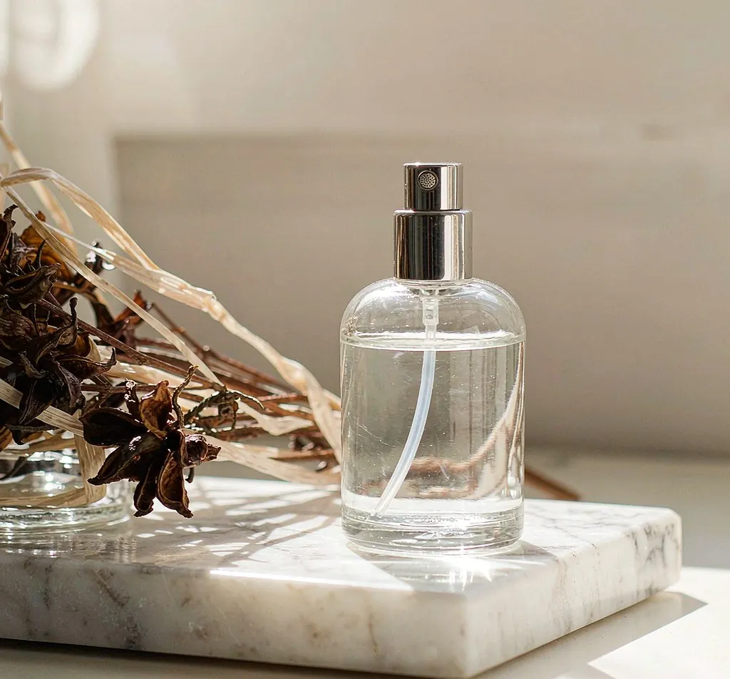 Clear glass atomizer spray bottle on a marble vanity tray with dried flowers