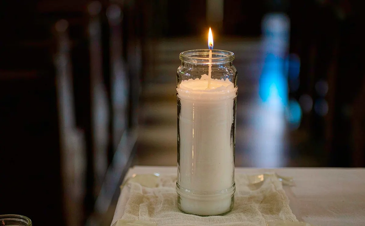 Lit white 7-day prayer candle burning inside a tall clear glass jar on an altar