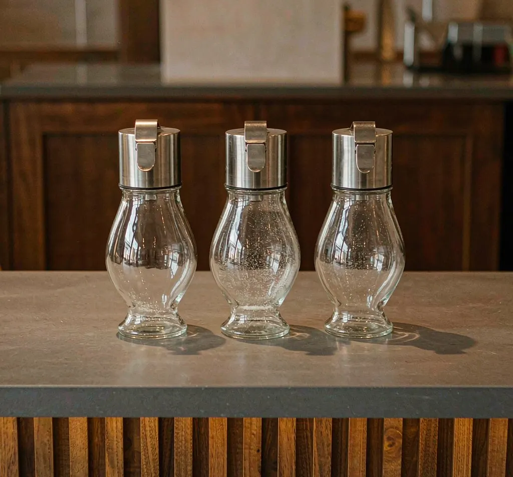 Glass sugar dispenser bottles with stainless steel pourer lids on cafe counter