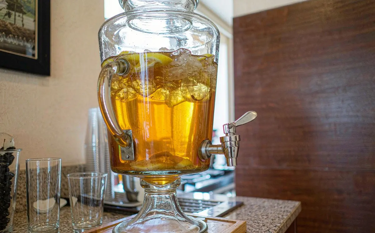 Glass beverage dispenser with iced tea and lemon on a buffet counter