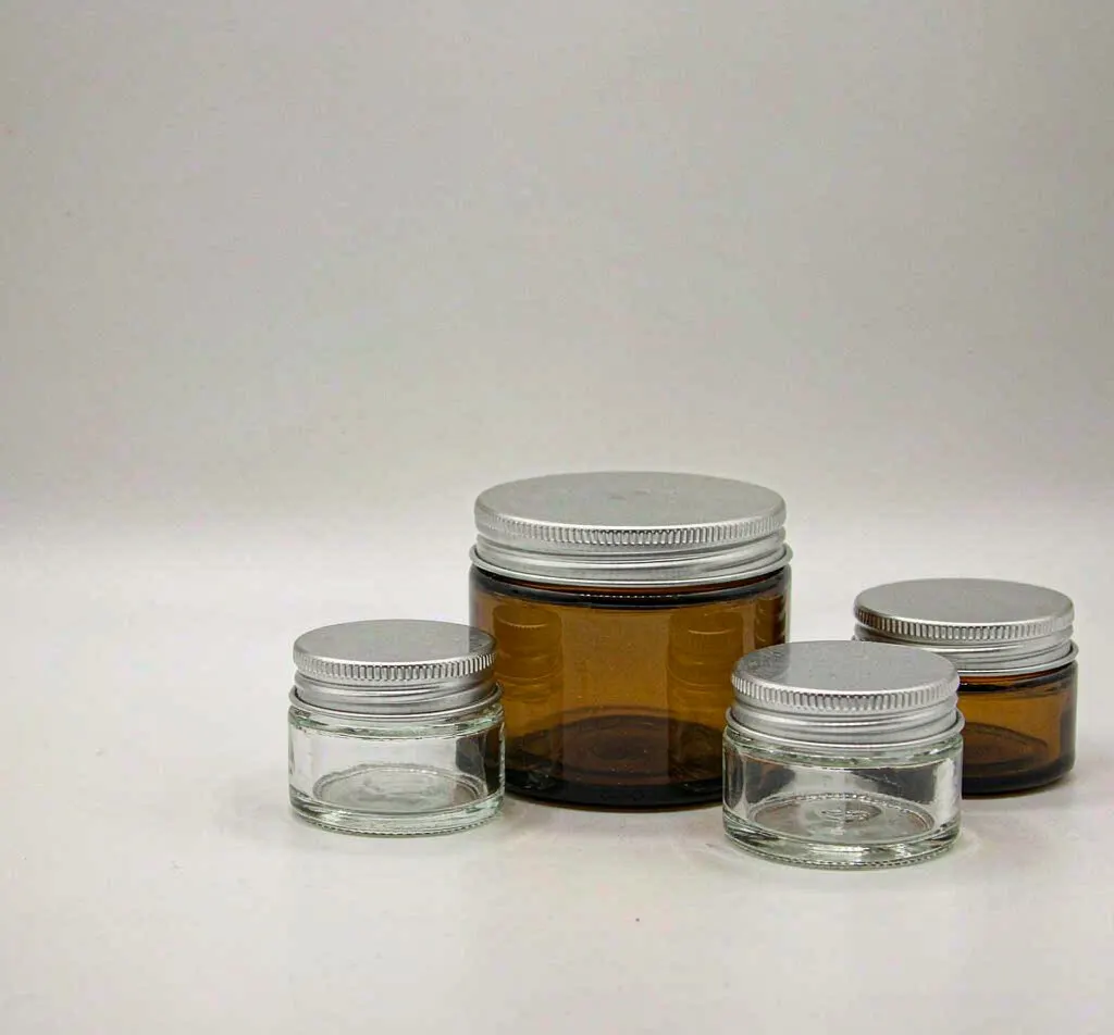 Clear and amber glass salve jars with silver aluminum lids in graduated sizes