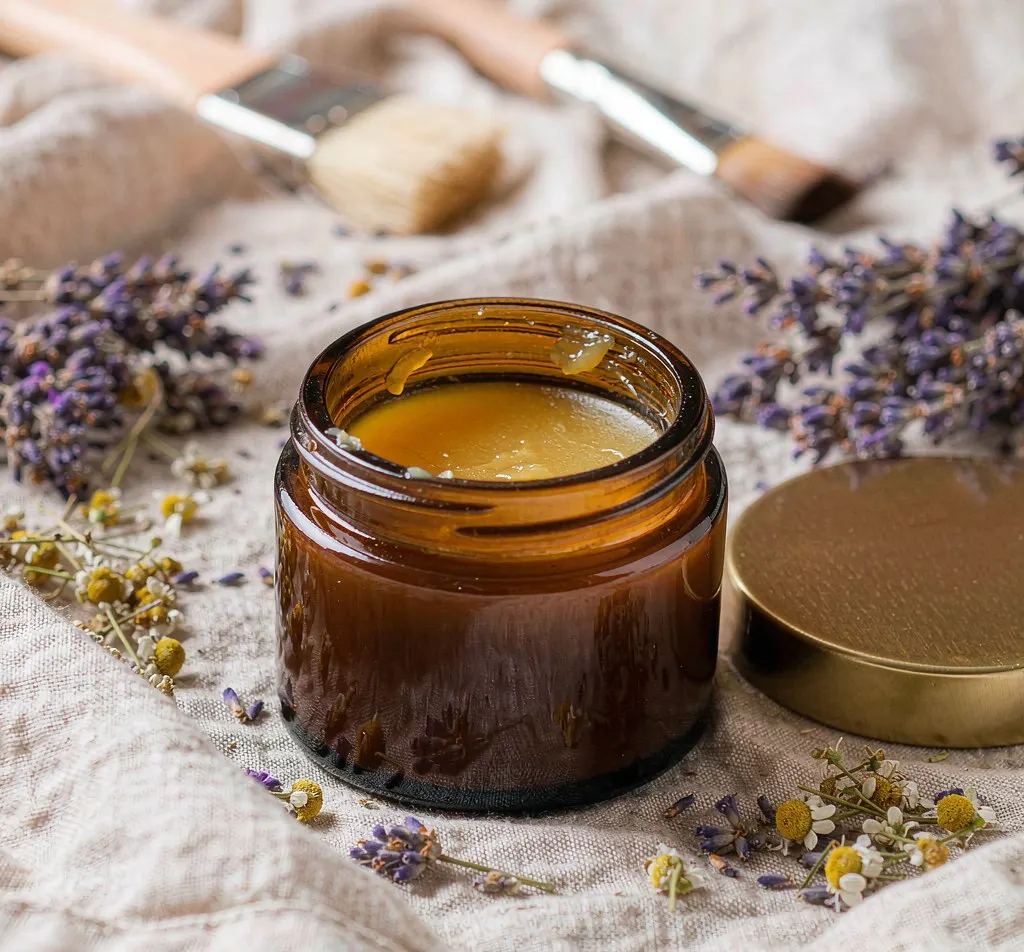 Open amber glass salve jar with golden balm and dried lavender