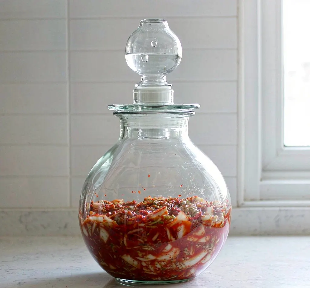 Glass fermentation jar with kimchi and glass airlock on a kitchen counter