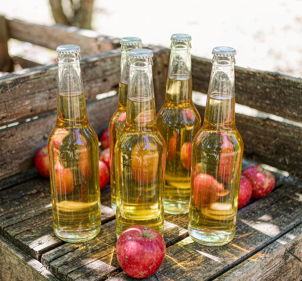Clear glass cider bottles with golden cider on a rustic orchard table