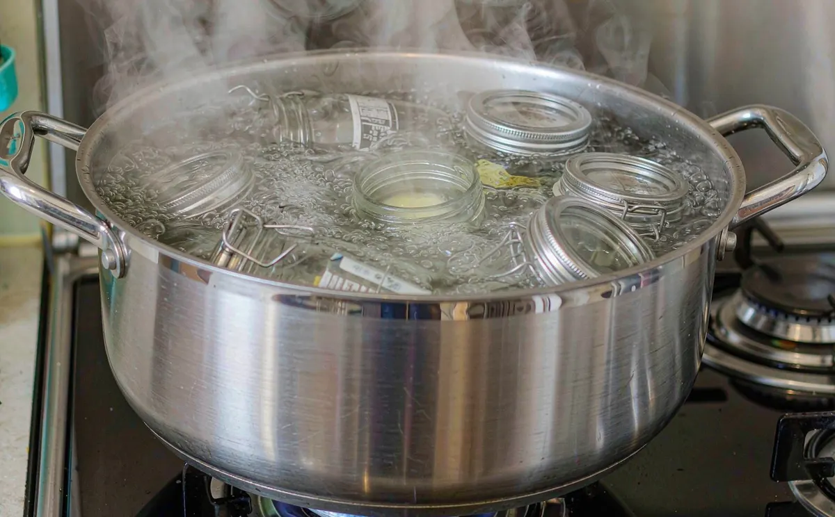Glass jars boiling in a stainless steel pot on a gas stove