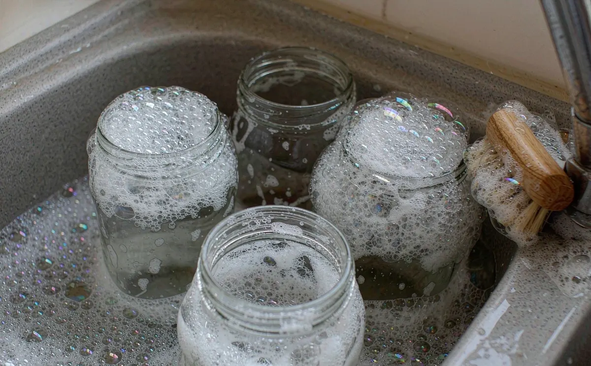 Glass jars soaking in a sink of hot soapy water for washing