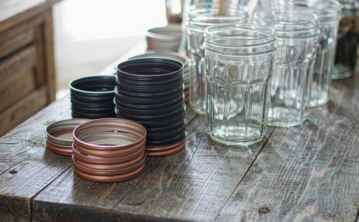 Canning lids and screw bands stacked neatly on a wooden table beside empty jars