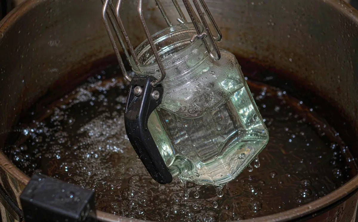 Jar lifter tongs lifting a dripping glass jar out of a water pot